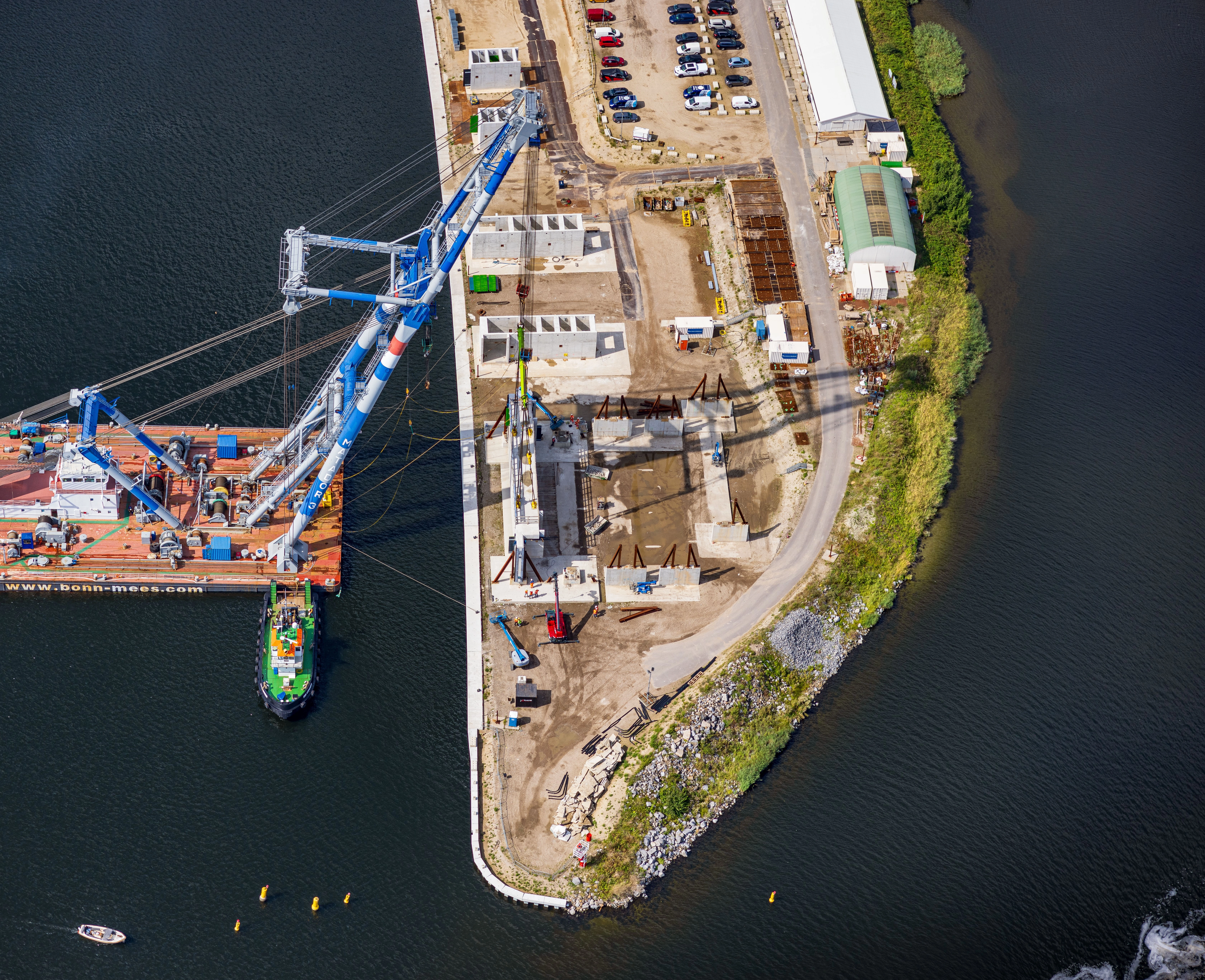 Luchtfoto van bouwplaats aan water met grote kraan op ponton, schepen en constructie-elementen voor zoutdam IJmuiden.