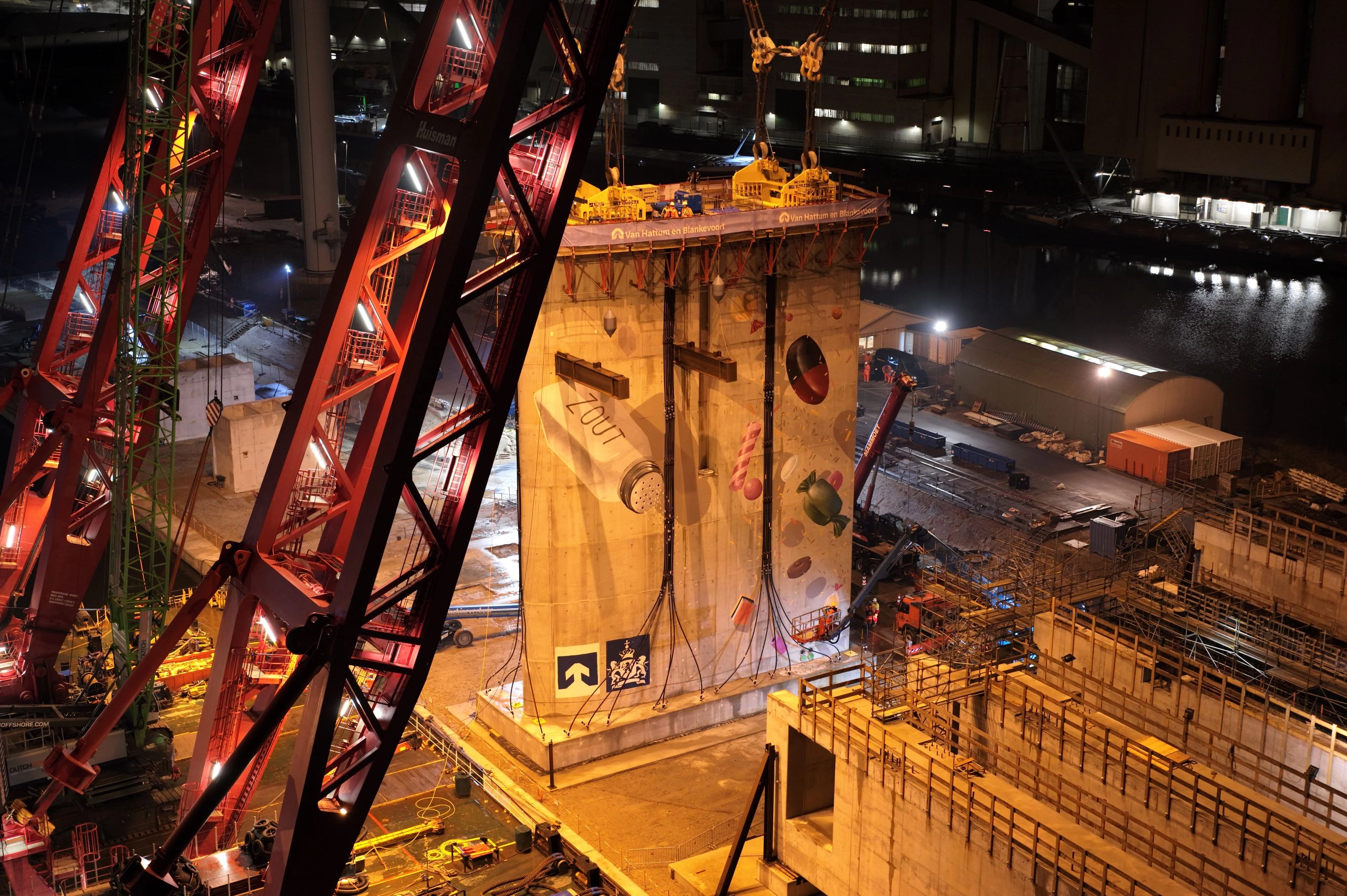 Nachtelijke bouwplaats met verlichte betonnen pijler, hijskranen en constructiemateriaal tijdens werkzaamheden aan zoutdam.