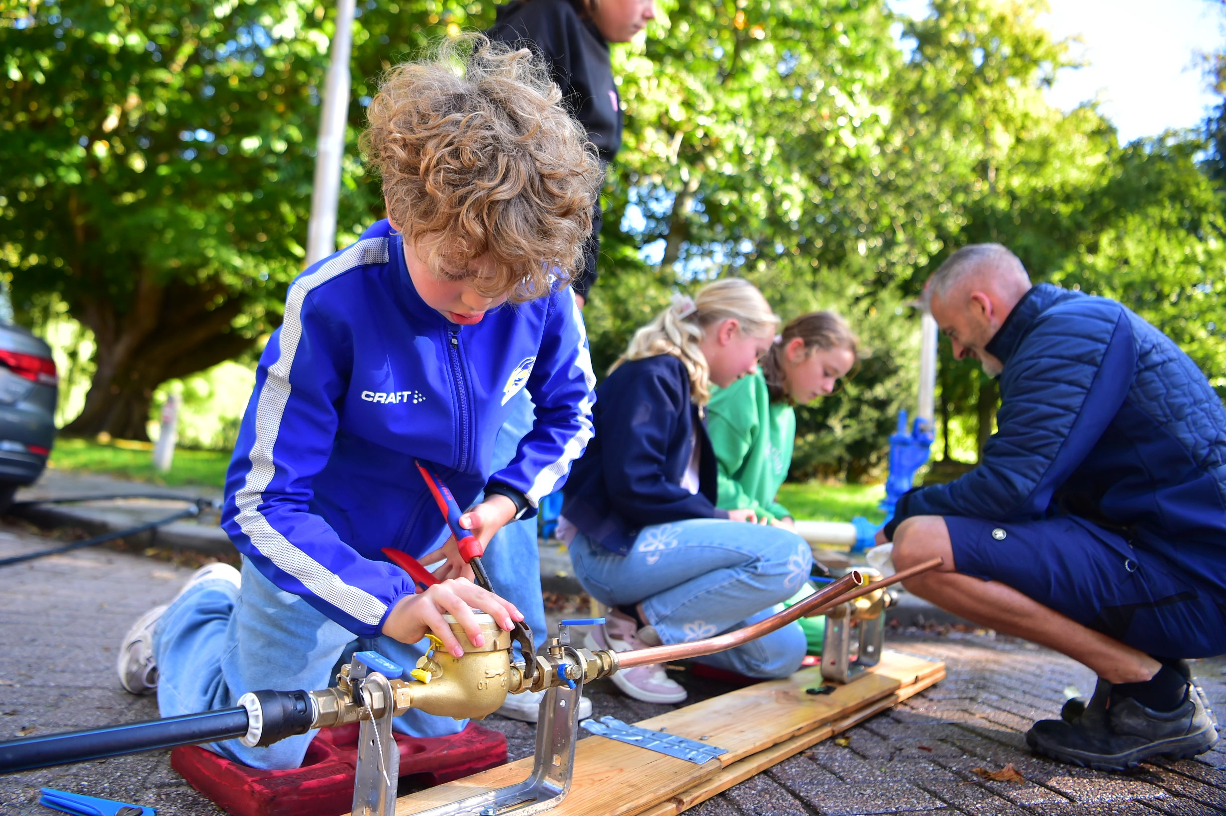 Leerlingen werken buiten aan het monteren van waterleidingen onder toezicht van een volwassene.