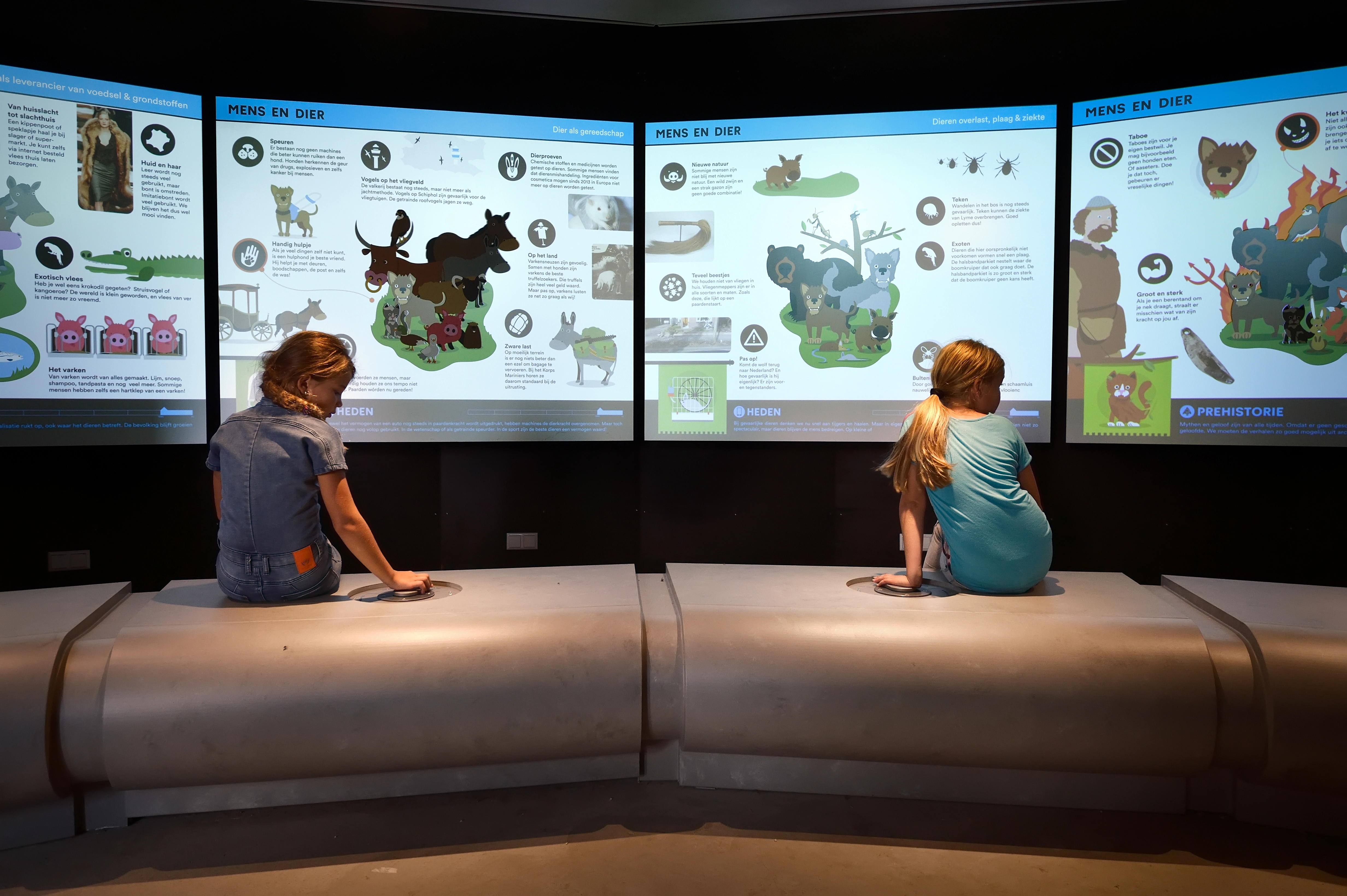 Twee kinderen bekijken informatieschermen over mens-dier relaties door de tijd heen.