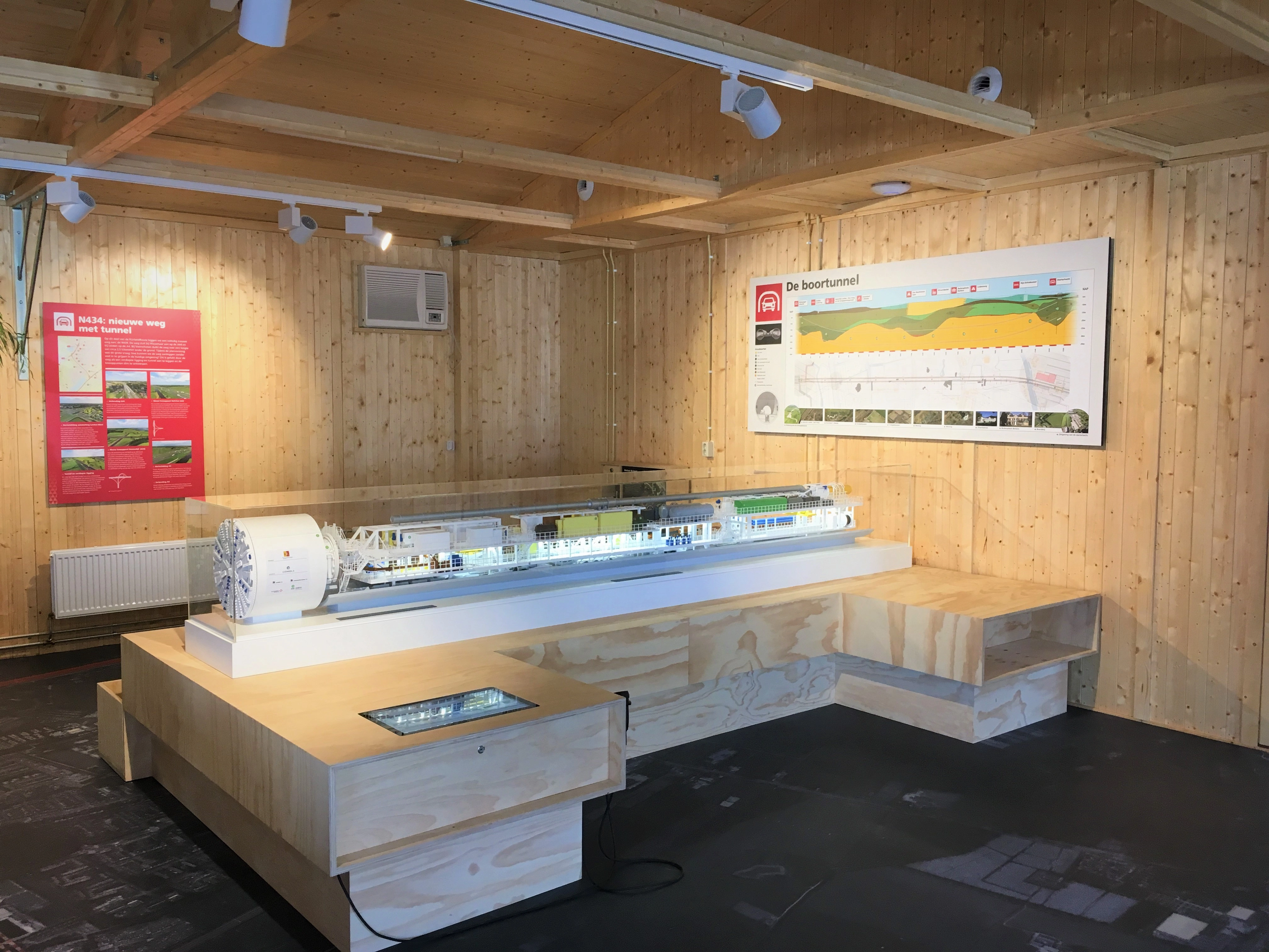 een houten platform met daarop een miniatuur. aan de muur hangen informatieve posters