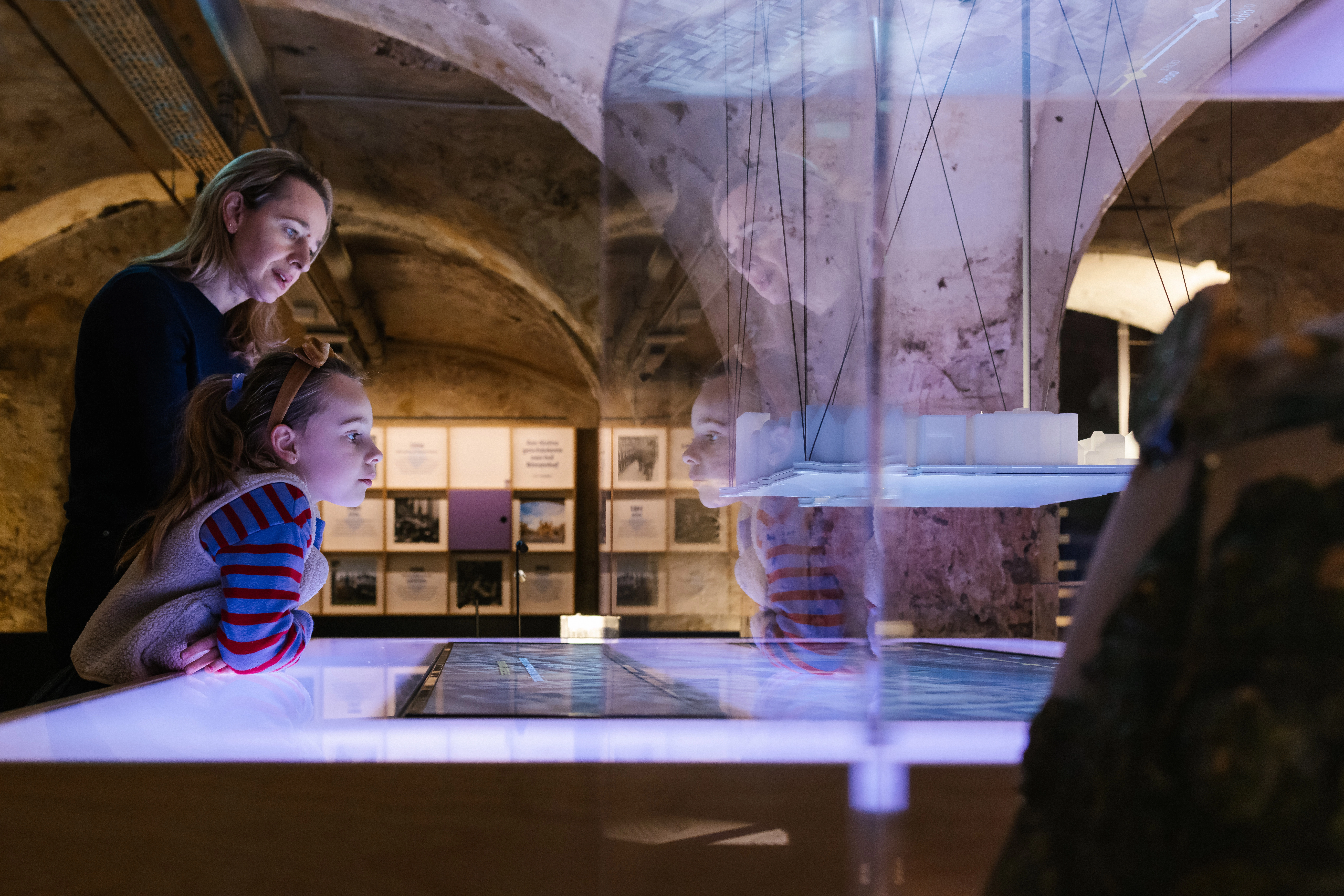 Interactieve maquette van het Binnenhof op een verlichte tafel, met bezoekers die details observeren in een historische kelderruimte.