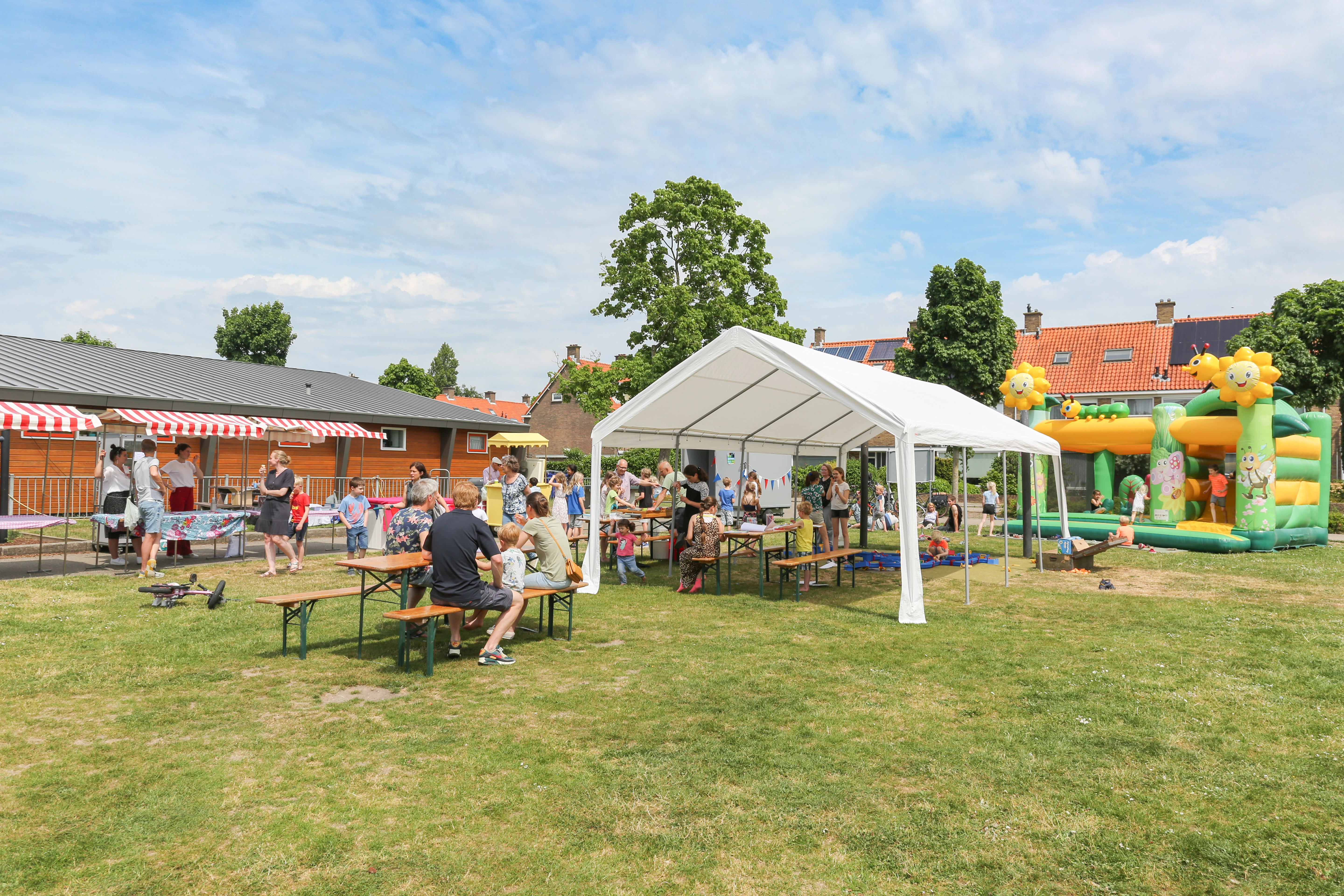 In een park staat een partytent, springkussen en verschillende kraampjes waar bewoners samenkomen