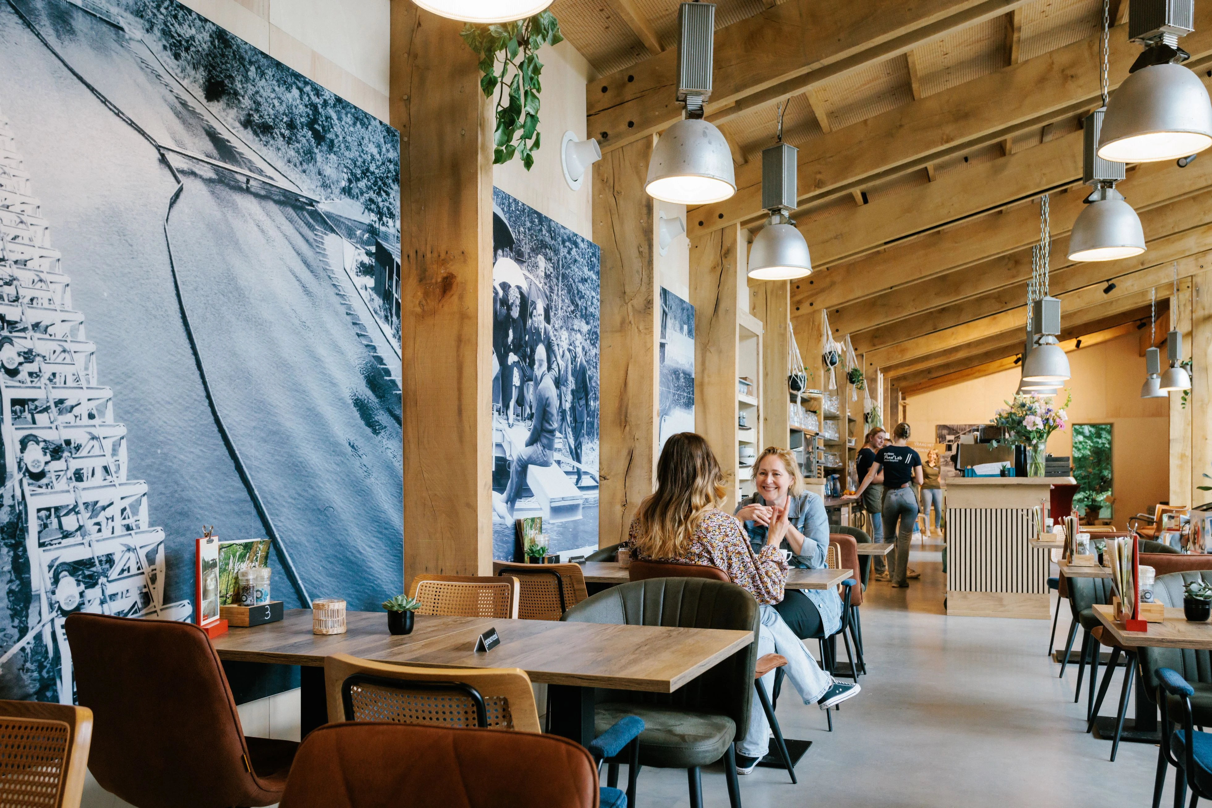 Een ruimte met meerdere tafels en stoelen waarbij je twee mensen aan een tafel tegenover elkaar ziet zitten