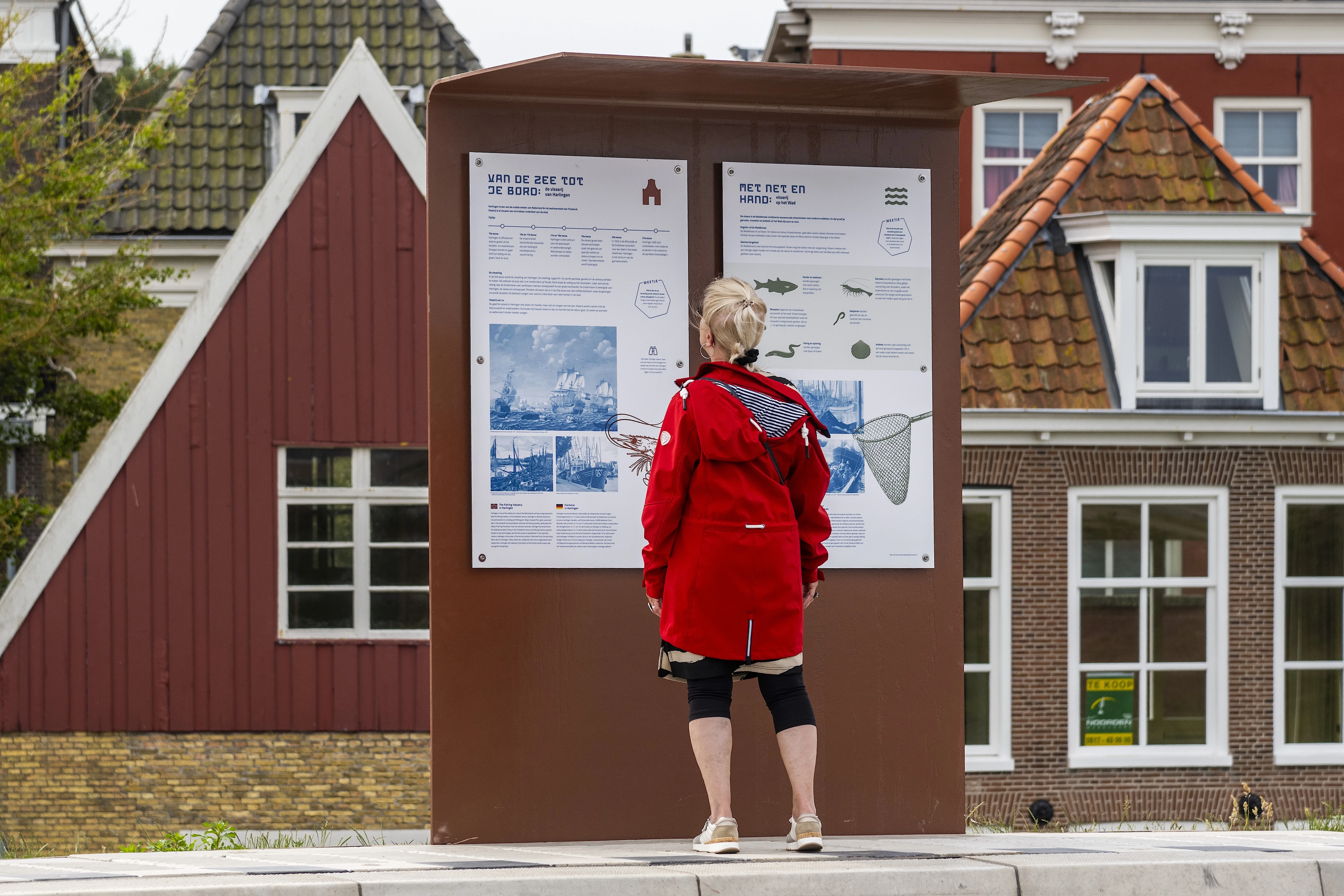 Een vrouw voor twee informatieve borden op de boulevard van Harlingen